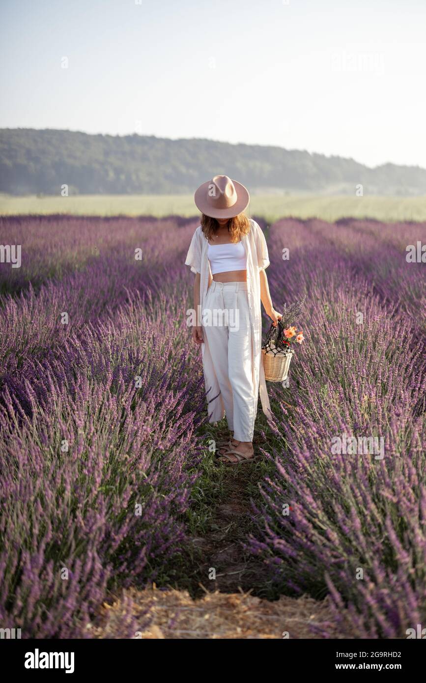 Giovane donna in cappello che si trova sul campo di lavanda con bouquet di fiori e godere della bellezza della natura. Calma e concetto di consapevolezza. Spazio di copia Foto Stock