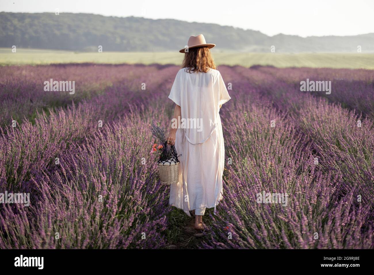 Giovane donna che si trova sul campo di lavanda con bouquet di fiori e godere della bellezza della natura. Calma e concetto di consapevolezza. Foto Stock