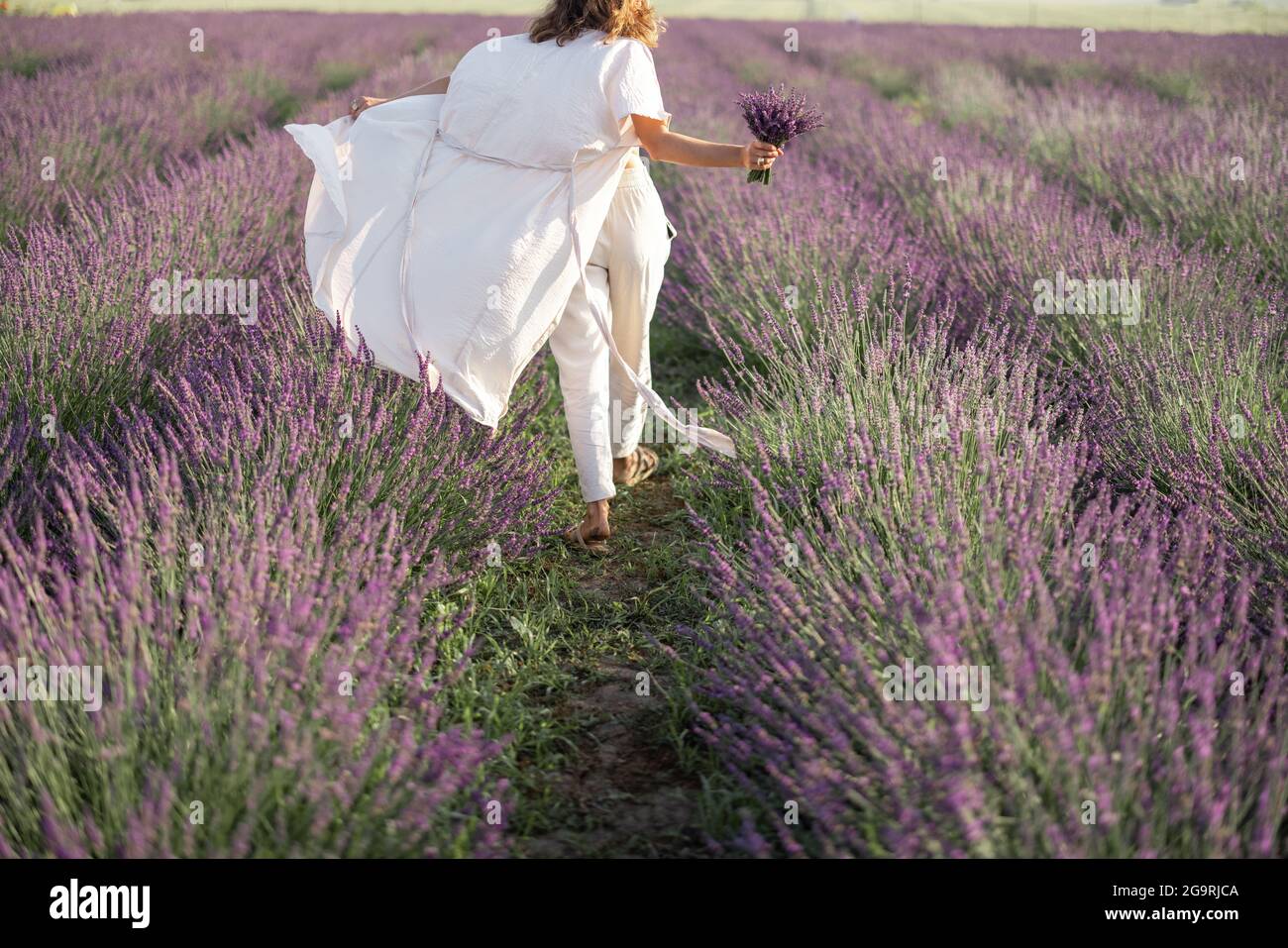 Giovane donna che corre sul campo di lavanda con bouquet di fiori violetti e godere della bellezza della natura. Calma e concetto di consapevolezza. Spazio di copia Foto Stock