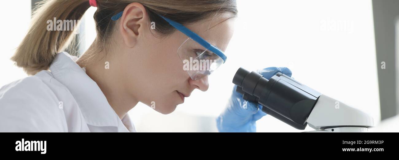 Donna scienziata con occhiali conduce la ricerca attraverso il microscopio Foto Stock