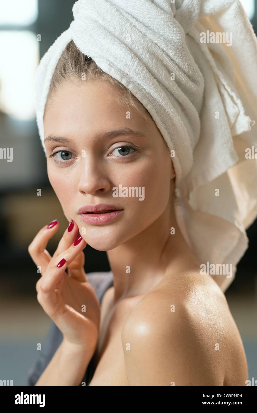 Giovane bella donna felice in pigiama grigio seta che applica cosmetici prodotto sulla sua faccia e godendolo al mattino dopo il bagno Foto Stock