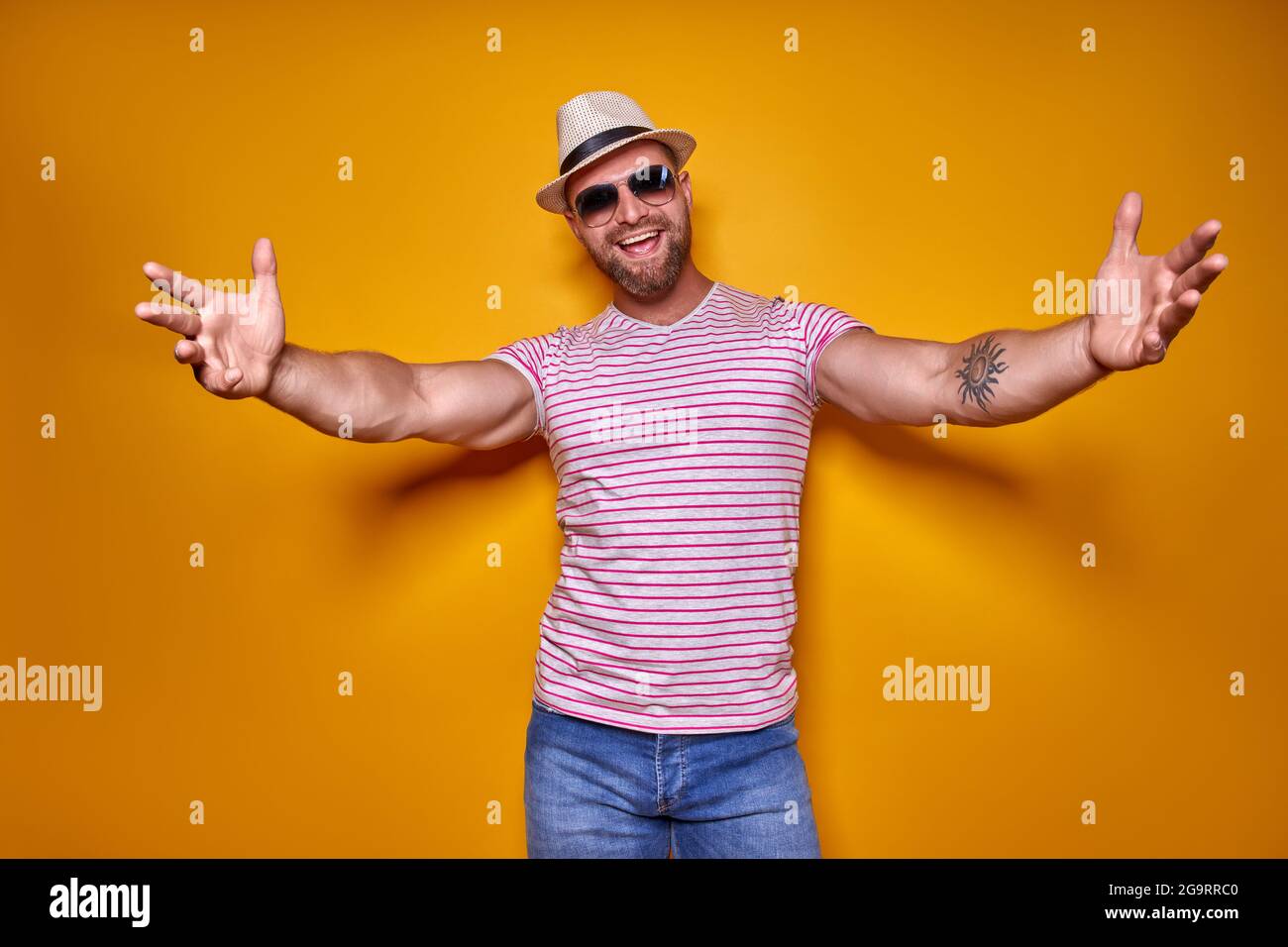 Avvicinati, mi abbraccio. Studio shot di positivo amichevole bearded uomo in trendy spogliato vestito e cappello che tira le mani verso la macchina fotografica, invitante Foto Stock