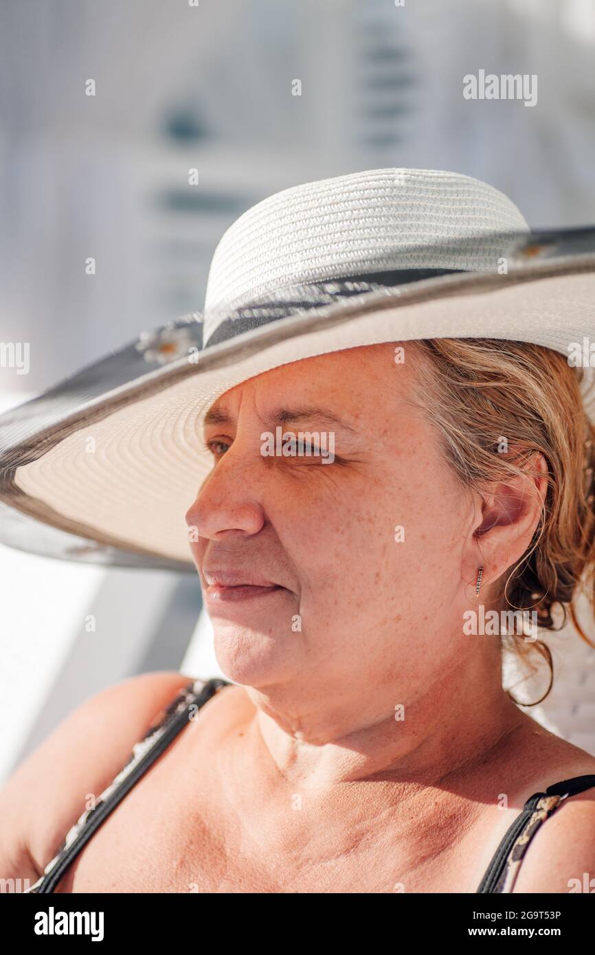 Una donna in un cappello di paglia. Profilo ritratto di una donna di charme in un cappello bianco di paglia che si rilassa sulla spiaggia al mare all'ombra Foto Stock