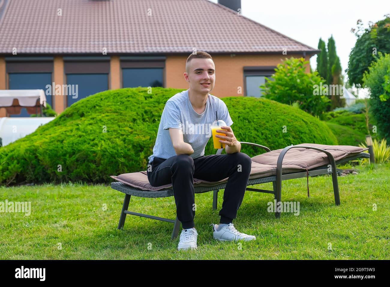 L'uomo con un braccio amputato si siede su un lettino e beve cocktail nel cortile Foto Stock