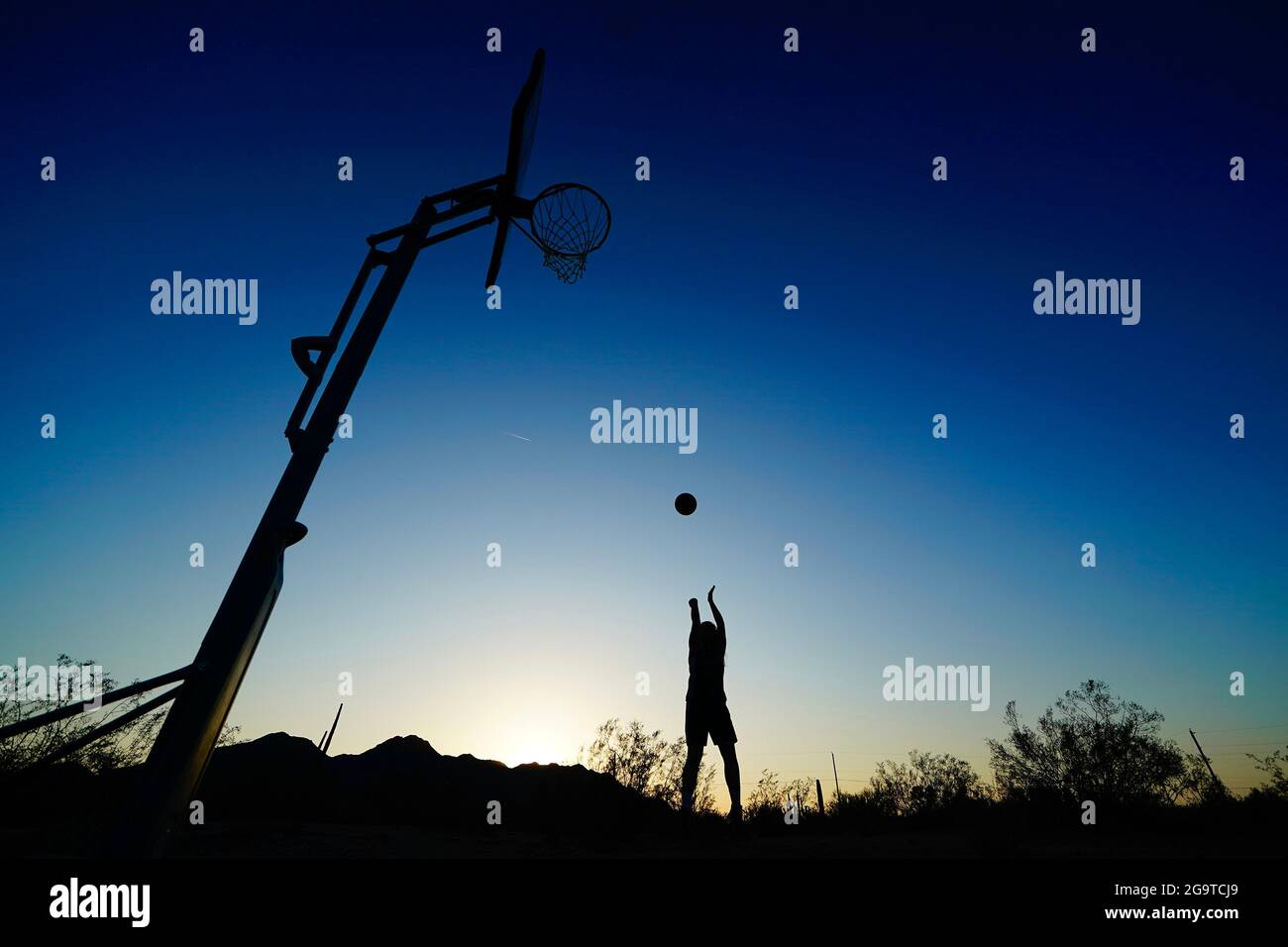 Una silhouette di un giocatore di basket che pratica il loro tiro nel mezzo del deserto durante il tramonto. Foto Stock