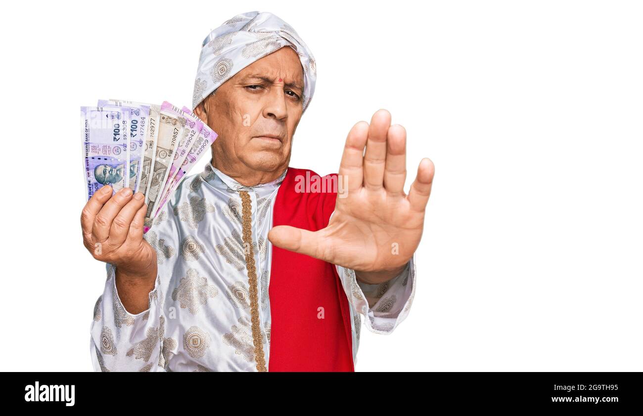 Uomo ispanico anziano che indossa costume sherwani tenendo in mano le banconote  di rupia indiane con mano aperta facendo segno di stop con espressione  seria e sicura, sfida Foto stock - Alamy