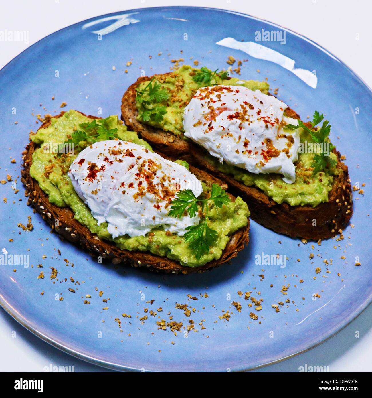 l'avocado è stato schiacciato su pane tostato a grani interi con uova biologiche in camicia su un piatto da portata Foto Stock