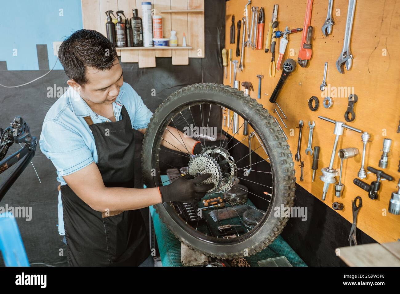 un meccanico di bicicletta in un grembiule controlla la ruota libera durante la riparazione di una ruota di bicicletta Foto Stock