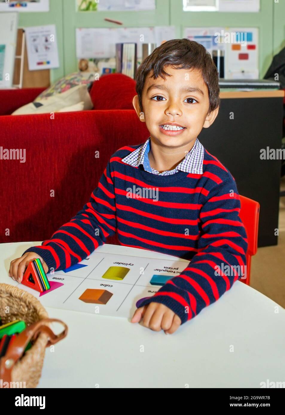 sorridente bambino seduto ad un tavolo di apprendimento forme Foto Stock