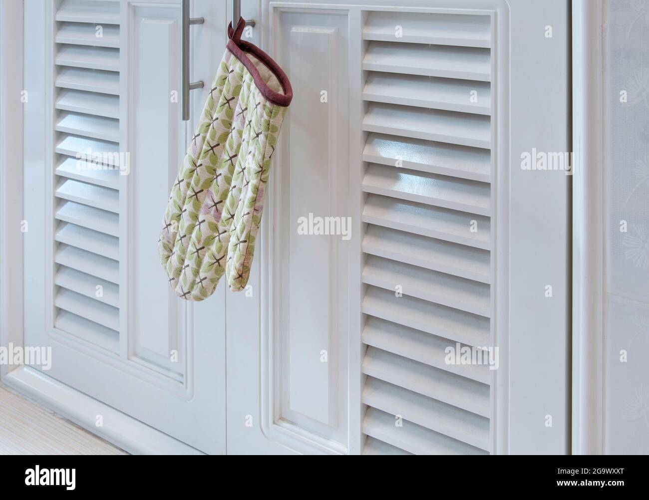 I guanti resistenti al calore nel modello a balestra sono appesi alla maniglia del cabinet sotto la barra del banco in cucina, vista font per il centro benessere copia Foto Stock