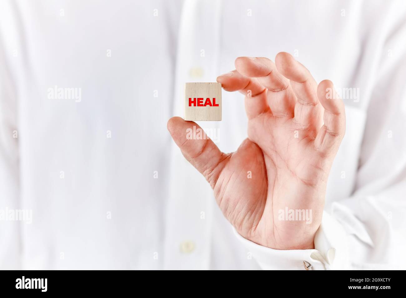 La mano del guaritore tiene un cubo di legno con la parola guarire. Medicina alternativa e concetto di guarigione. Foto Stock