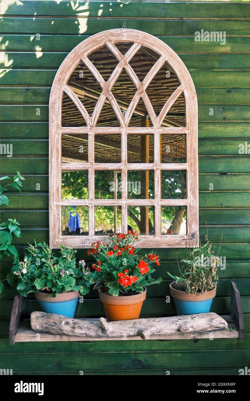 Specchio decorativo ad arco appeso su una parete di legno verde con fiori  colorati nei vasi di fiori. Decorazioni in stile country Foto stock - Alamy