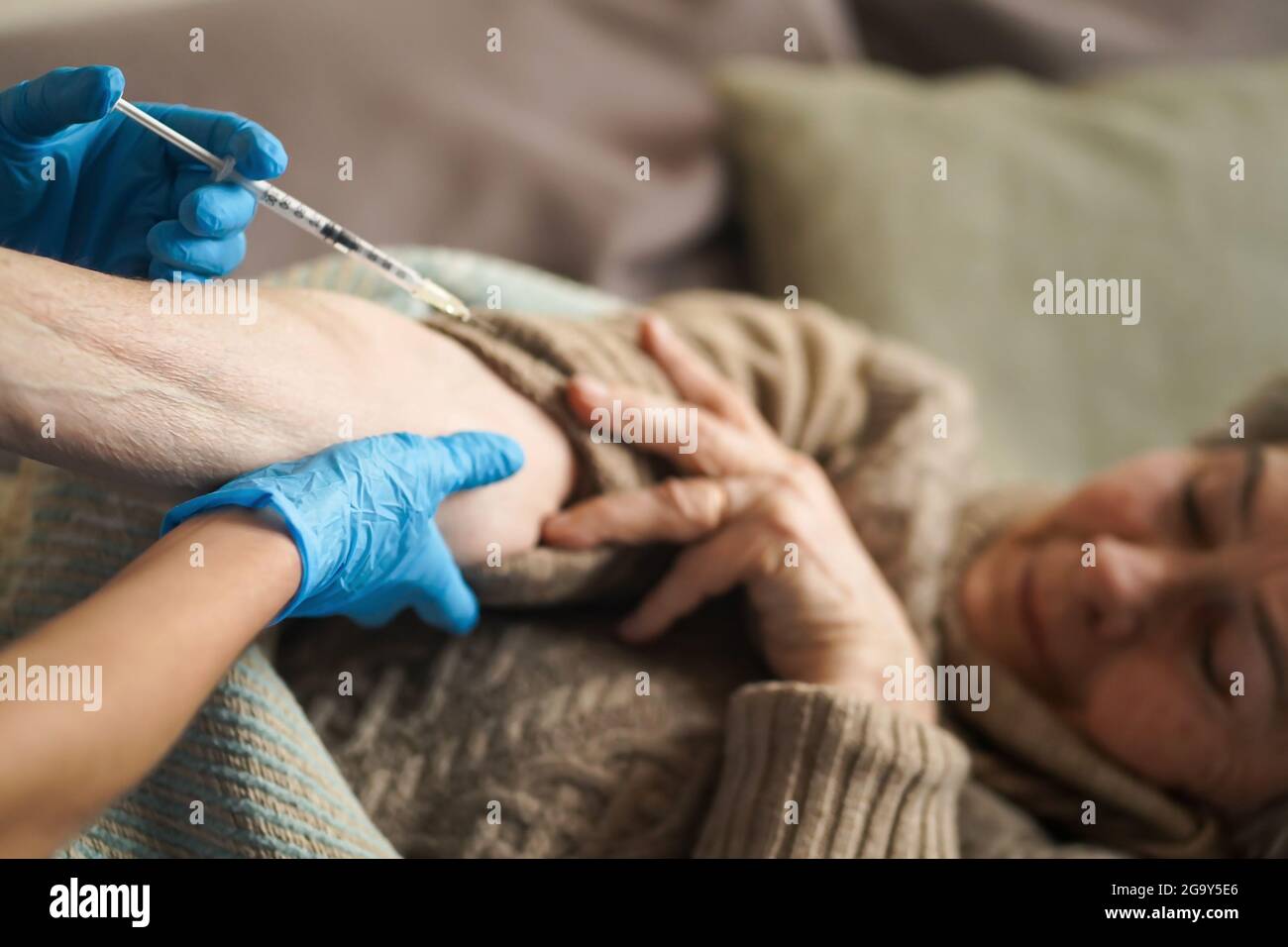 L'infermiere effettua un'iniezione con il vaccino al paziente a casa. Foto Stock