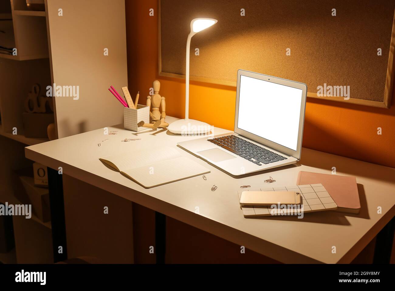 Ambiente di lavoro elegante con lampada luminosa e un moderno computer portatile vicino a una parete colorata di notte Foto Stock
