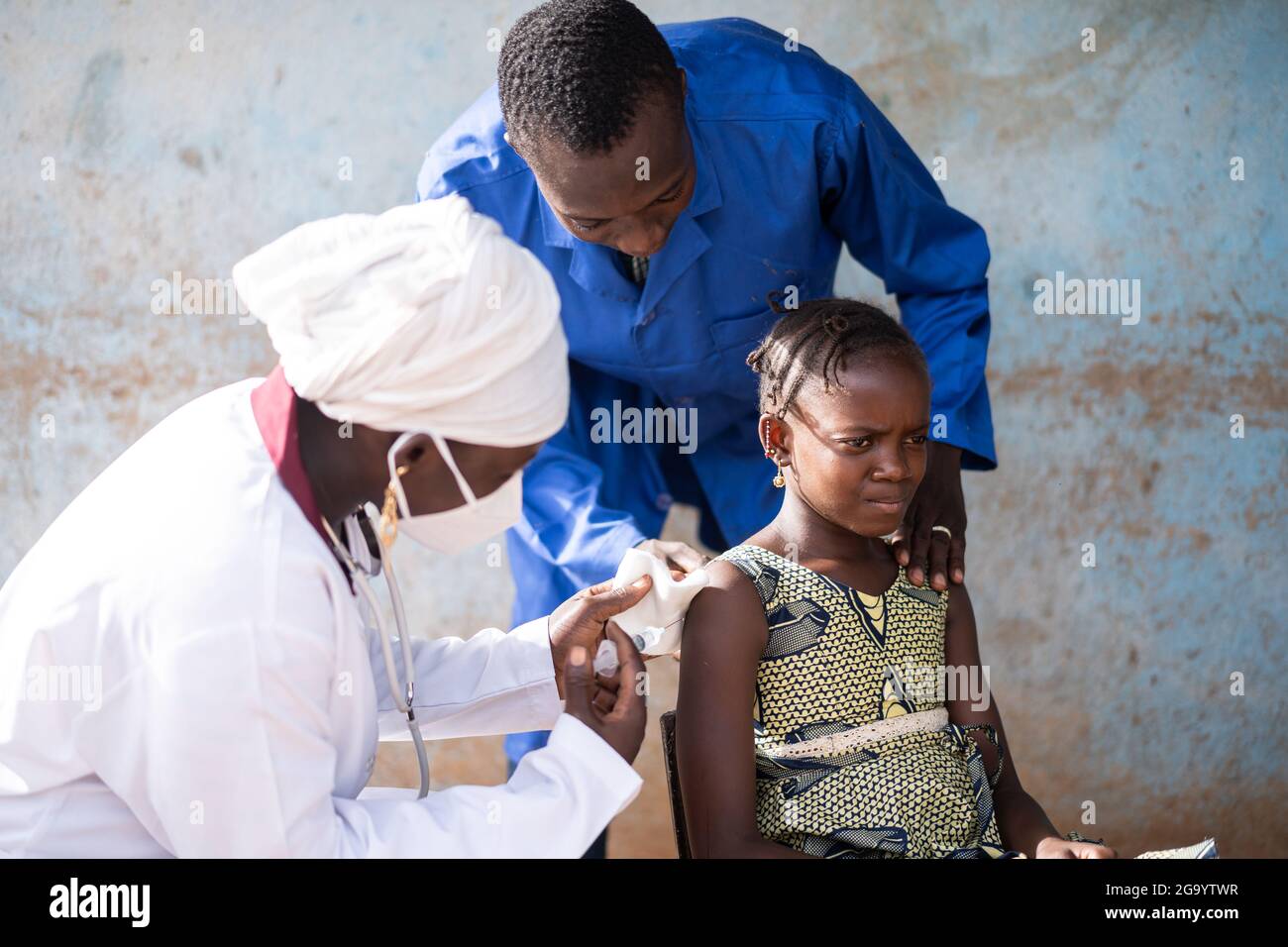 In questa immagine una piccola ragazza africana molto preoccupata quasi spaventa seduta sta beeing vaccinata e confortata da un paio di profes neri di sanità Foto Stock