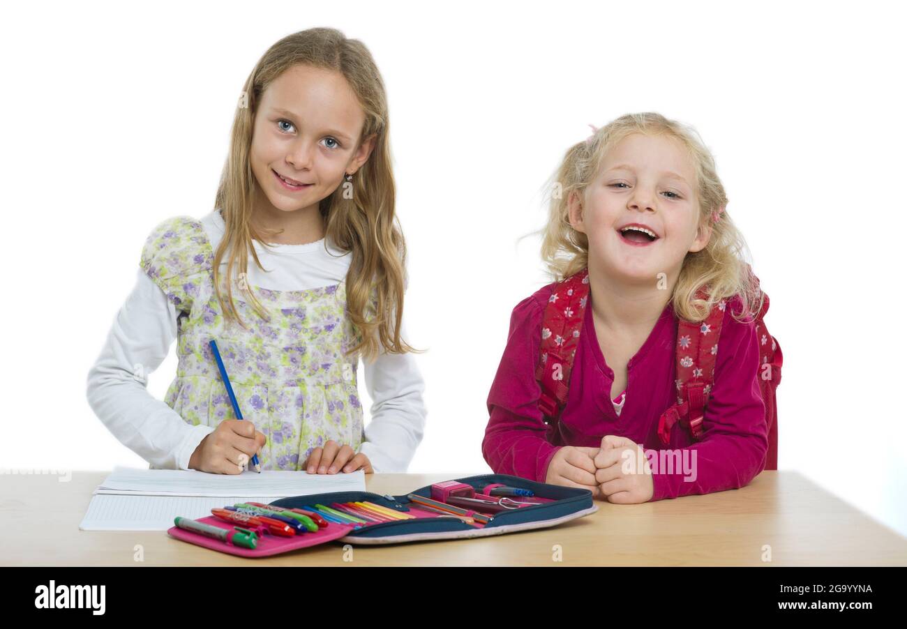 due sorelle felici, kindergartner con zaino e studente di scuola elementare in una scrivania Foto Stock