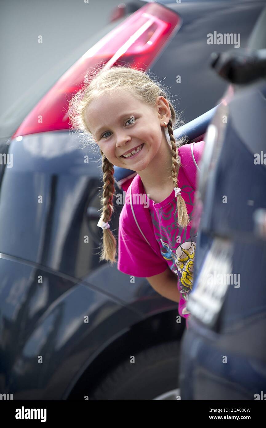 Felice studentessa elementare che si apita tra le auto parcheggiate, Germania Foto Stock