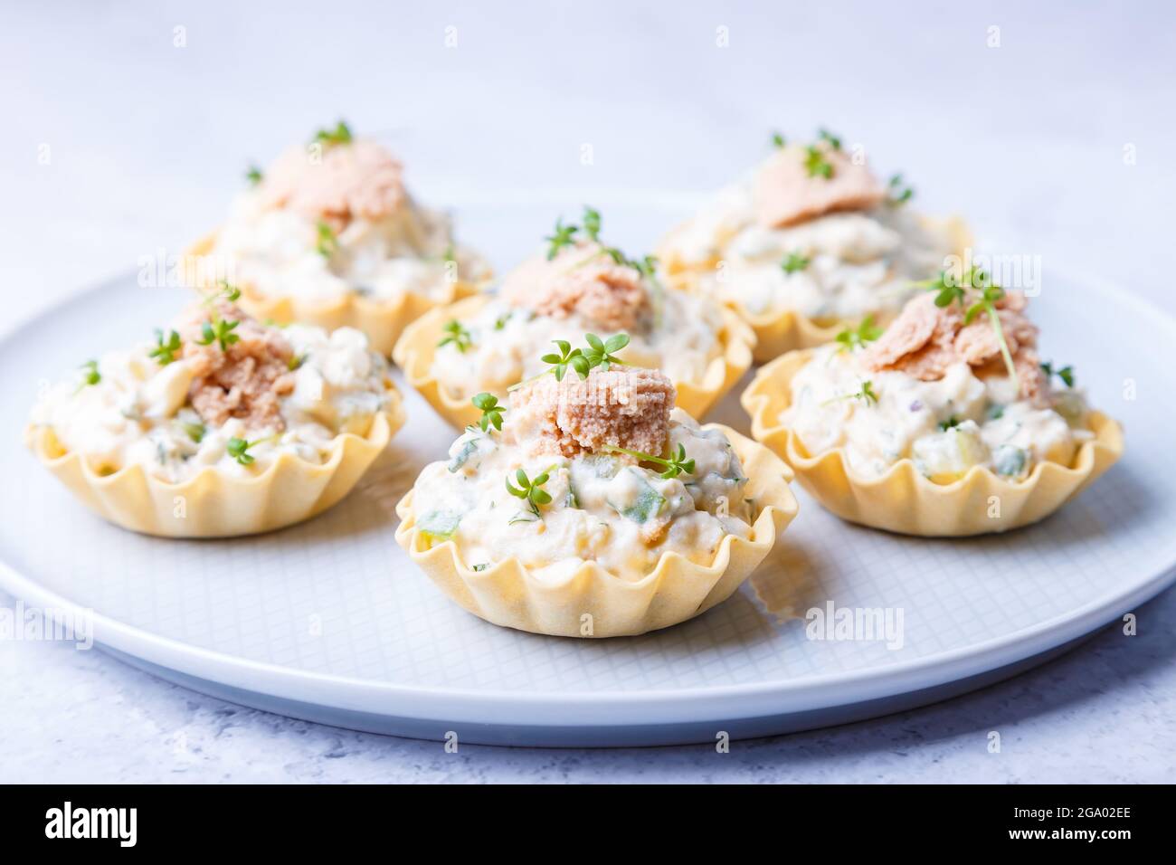 Tartlet ripieni di fegato di merluzzo, caviale di merluzzo, cetriolo e micrograni. Antipasto tradizionale a base di porpora fredda in un cestino di pasticceria. Primo piano. Foto Stock