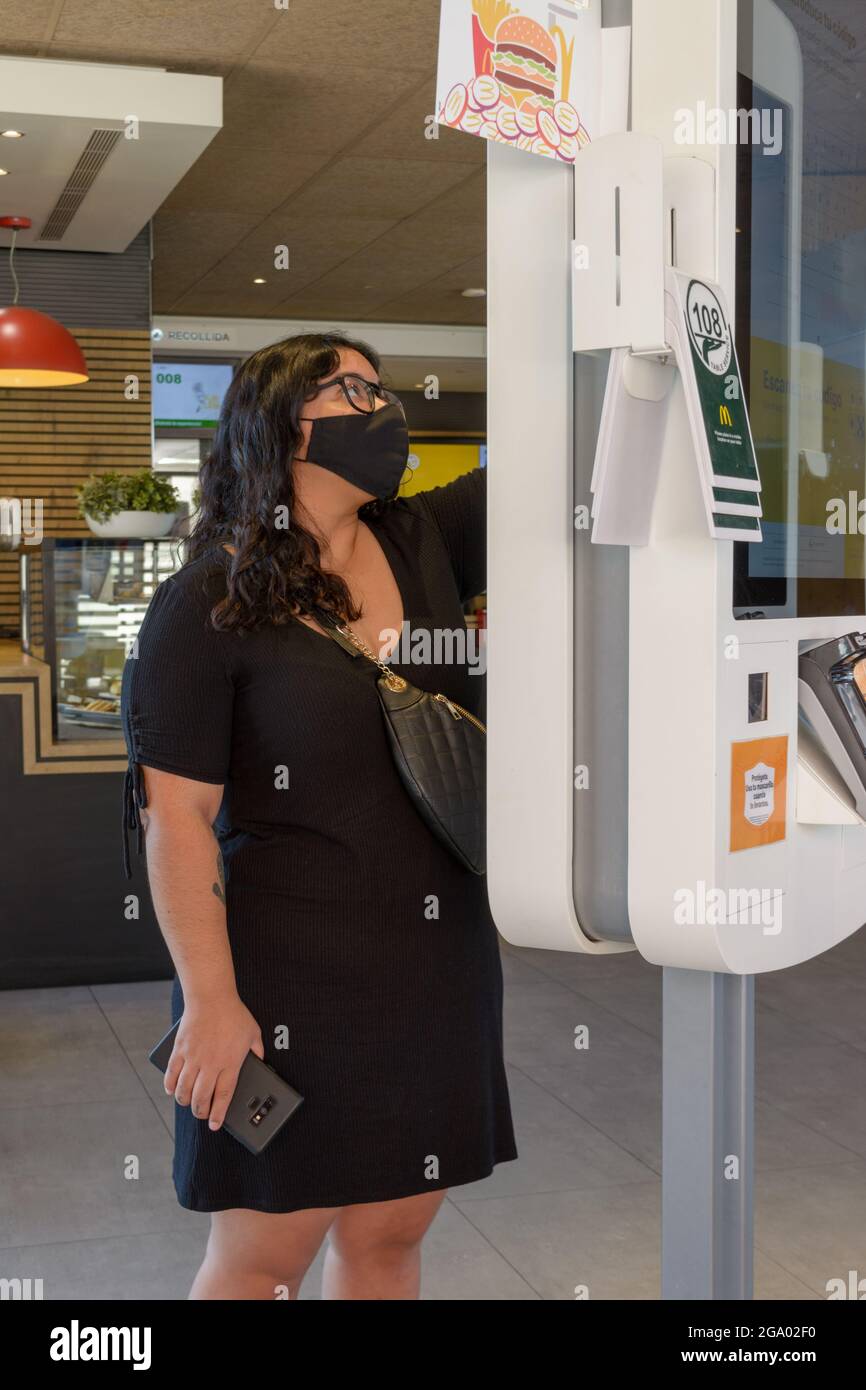 Mallorca, Spagna, 07-27-2021: Giovane donna che effettua un ordine su un touch screen con una maschera nel ristorante fast food di Macdonald nell'era post-pandemica, Foto Stock