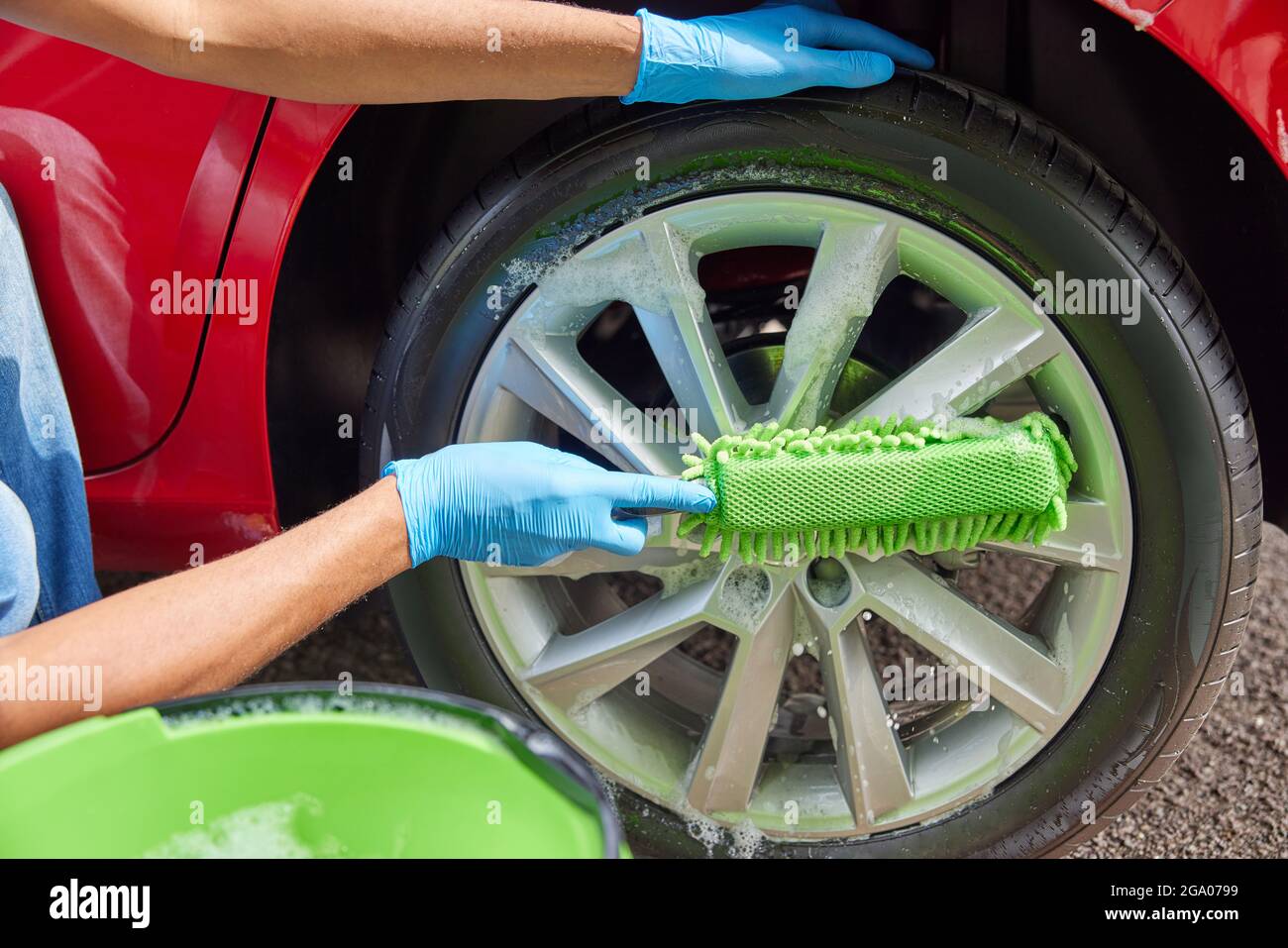 Primo piano di Man lavatrice ruote di auto durante Valet utilizzando secchio e spugna Foto Stock