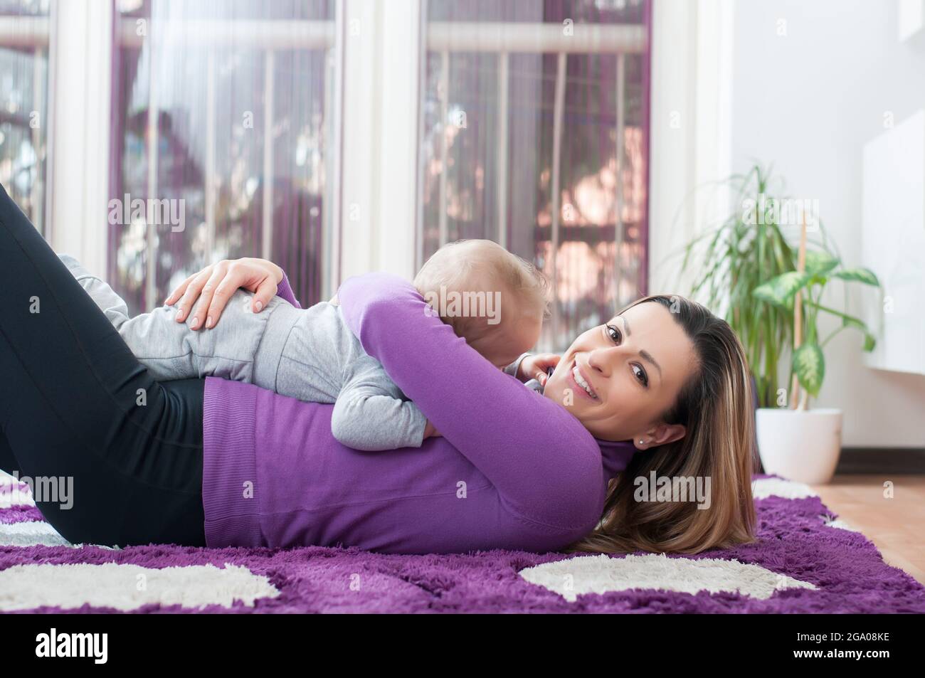 Madre felice che si stese sul pavimento e gioca con il suo bambino ragazzo Foto Stock