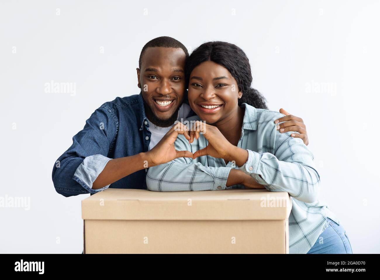 Immobiliare. Sposi Happy Black appoggiati su scatola di cartone, rendendo il cuore Gesture Foto Stock