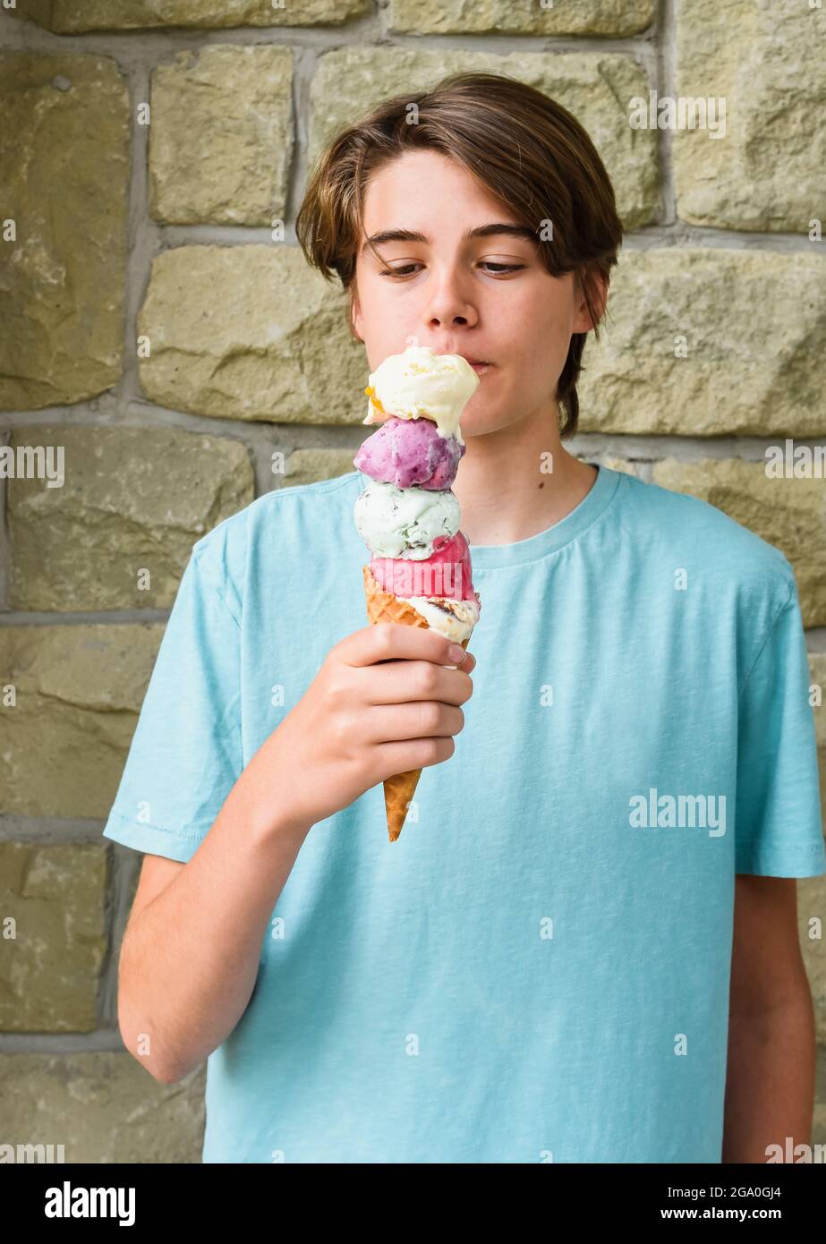 Teen boy che mangia un grande cono di gelato a paletta multipla all'esterno. Foto Stock