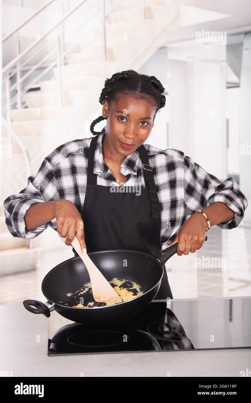 Sorridente afroamericana tenendo una padella profonda e mescolando le uova Foto Stock