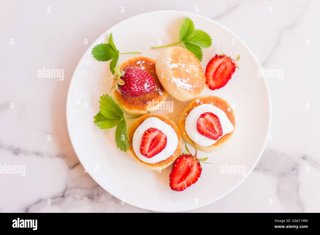 Deliziosa colazione del mattino. Frittella al formaggio. Pancake alla cagliata finemente decorati con fette di fragola e panna acida Foto Stock