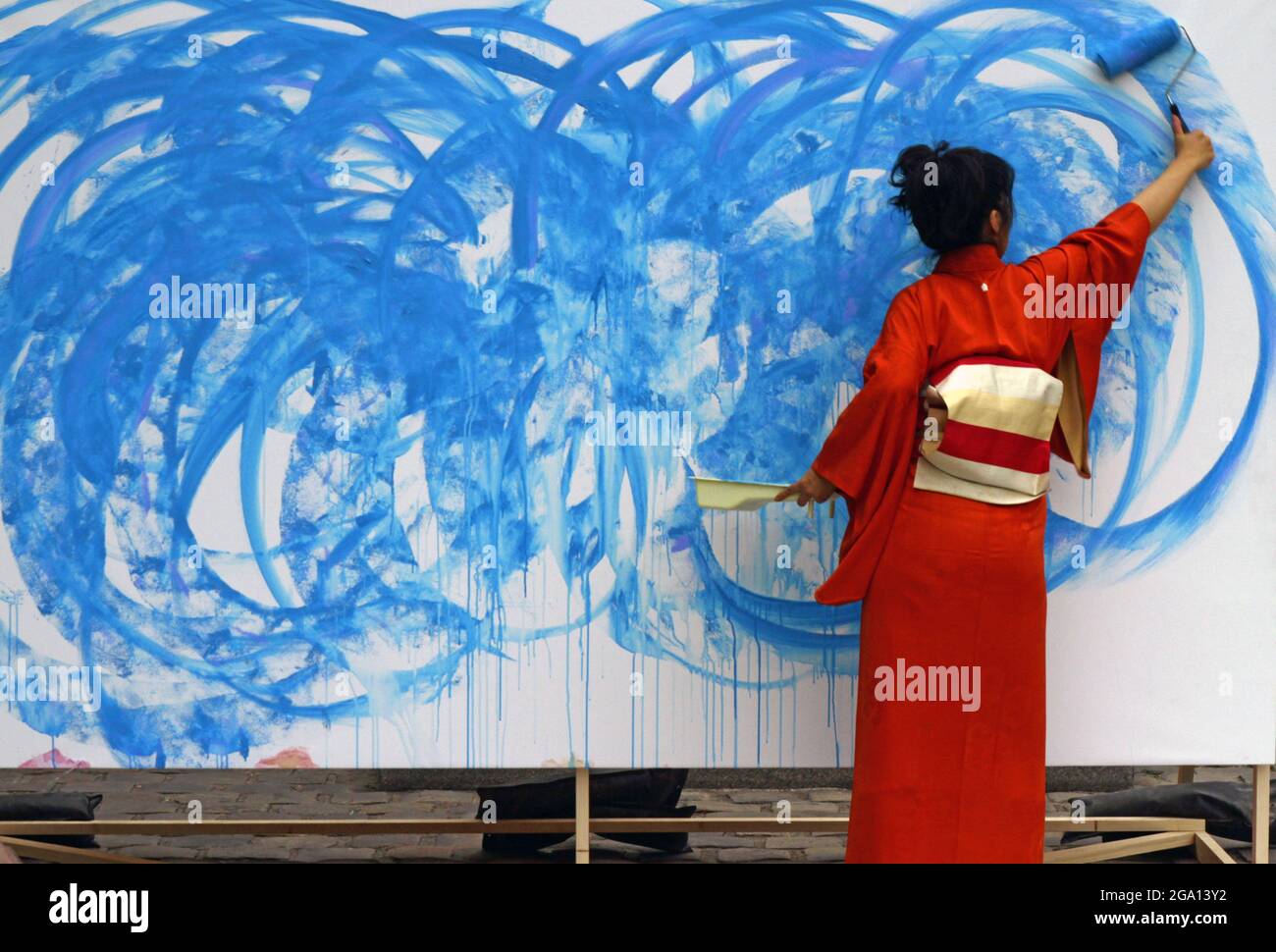 Vista posteriore di una femmina in un kimono rosso dipingendo una parete blu Foto Stock