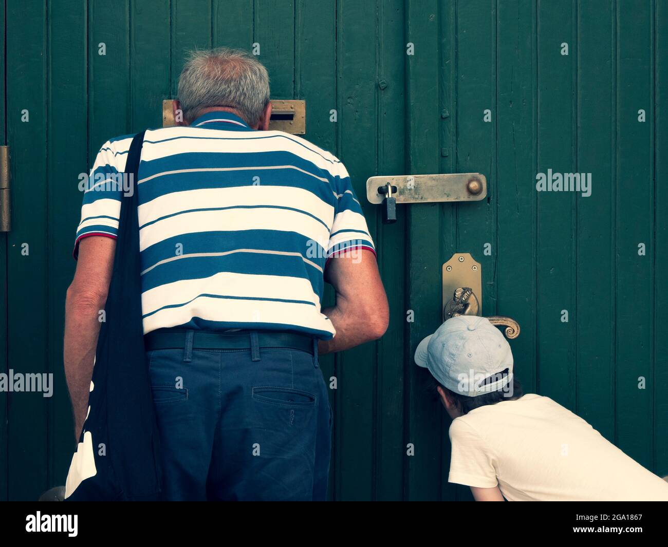 I bambini e gli anziani stanno guardando attraverso lo slot di posta e il buco della serratura, vista dal retro. Nonno e nipote vedono qualcosa di interessante Foto Stock