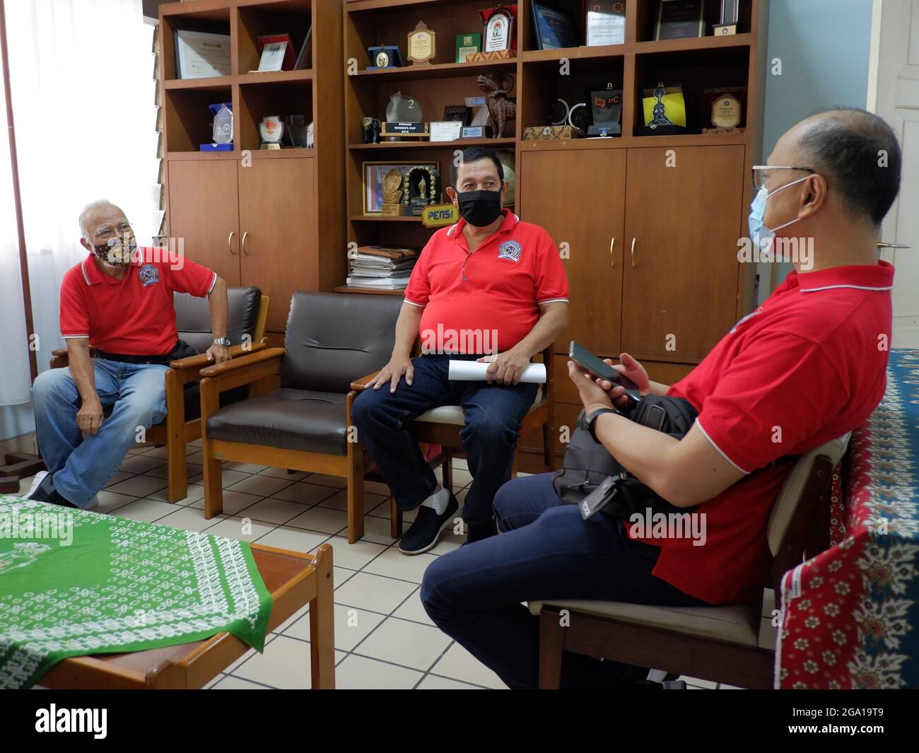 Tre uomini indossano maschera facciale e mantengono la distanza mentre si siede in un soggiorno. Foto Stock