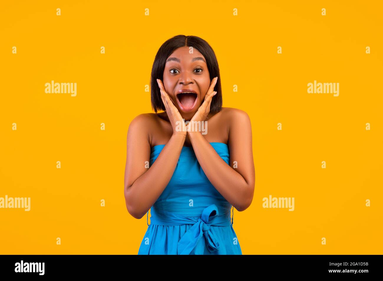 Eccitata donna afroamericana in abito estivo gridando in eccitazione, tenendo le mani vicino al viso, sfondo arancione Foto Stock