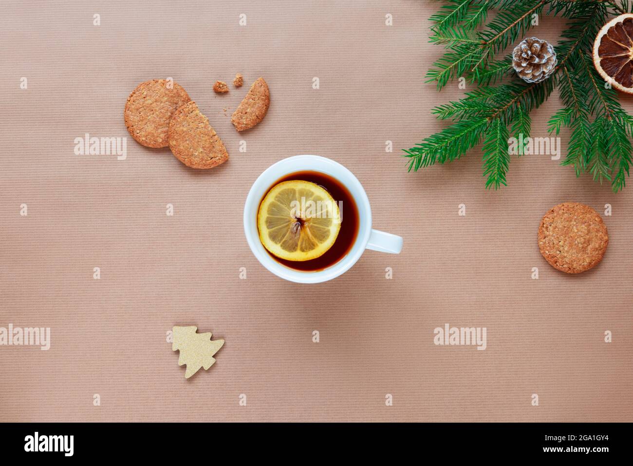 Rami dell'albero di Natale, tazza di tè con limone e biscotti su sfondo beige. Vista dall'alto, disposizione piatta, spazio per la copia. Foto Stock