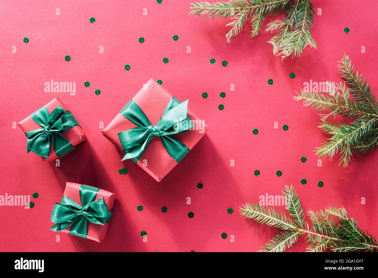 Natale e Capodanno di sfondo. Scatole regalo con archi verdi, rami di abete e confetti su sfondo rosso. Vista dall'alto, disposizione piatta. Foto Stock