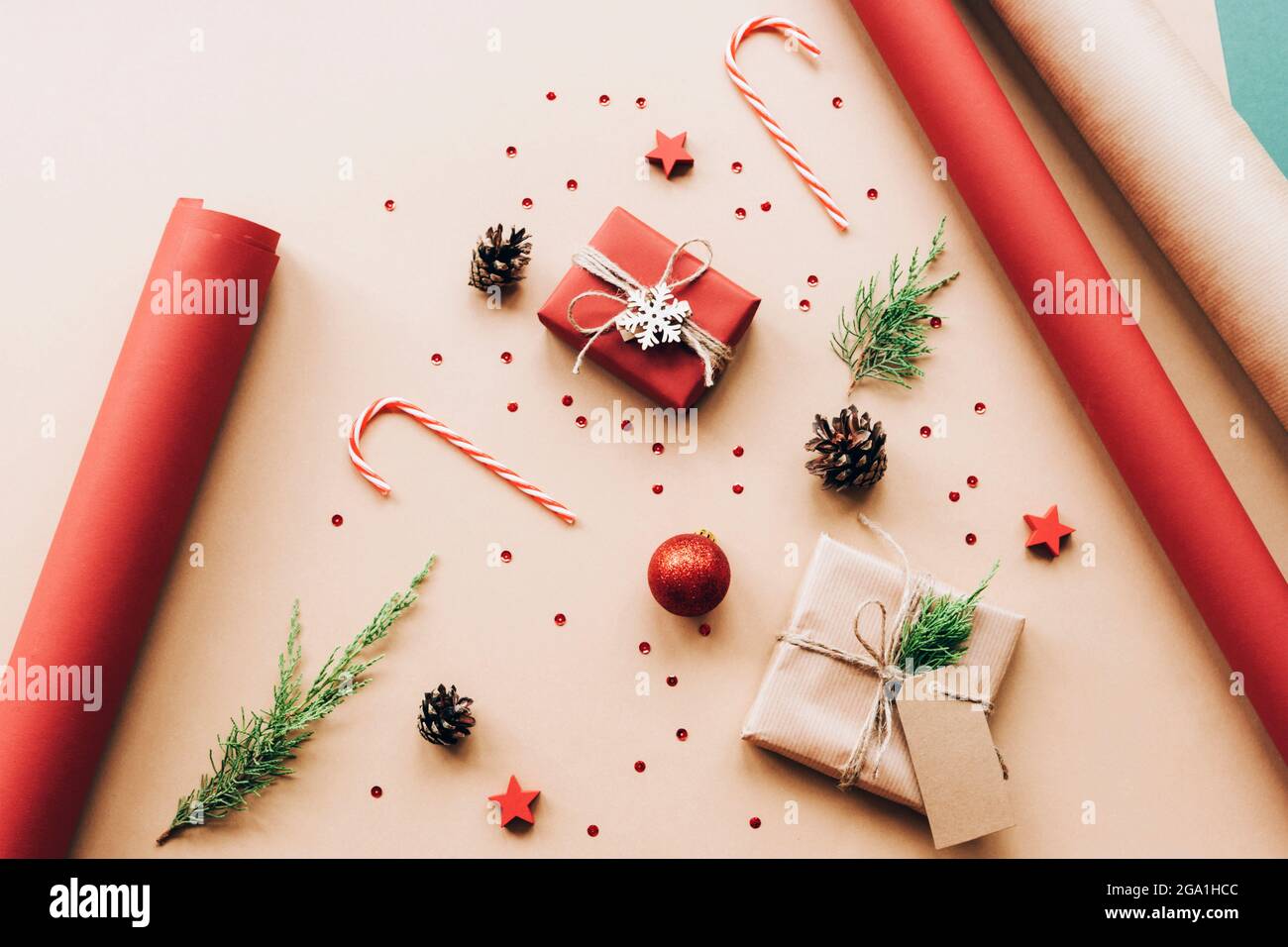 Scatole regalo, canne caramelle e rami di cipresso. Preparazione di Natale di regali su carta da artigianato beige. Concetto di nuovo anno. Vista dall'alto, disposizione piatta. Foto Stock