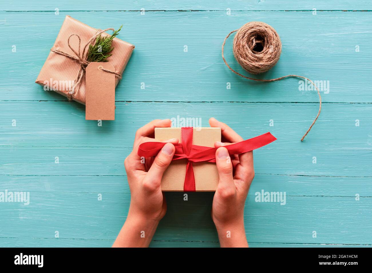 Sfondo di Natale con scatole regalo, matassa di corda su teal blu tavolo di legno. Preparazione per le vacanze. Vista dall'alto, disposizione piatta. Le mani della ragazza che tengono il regalo Foto Stock