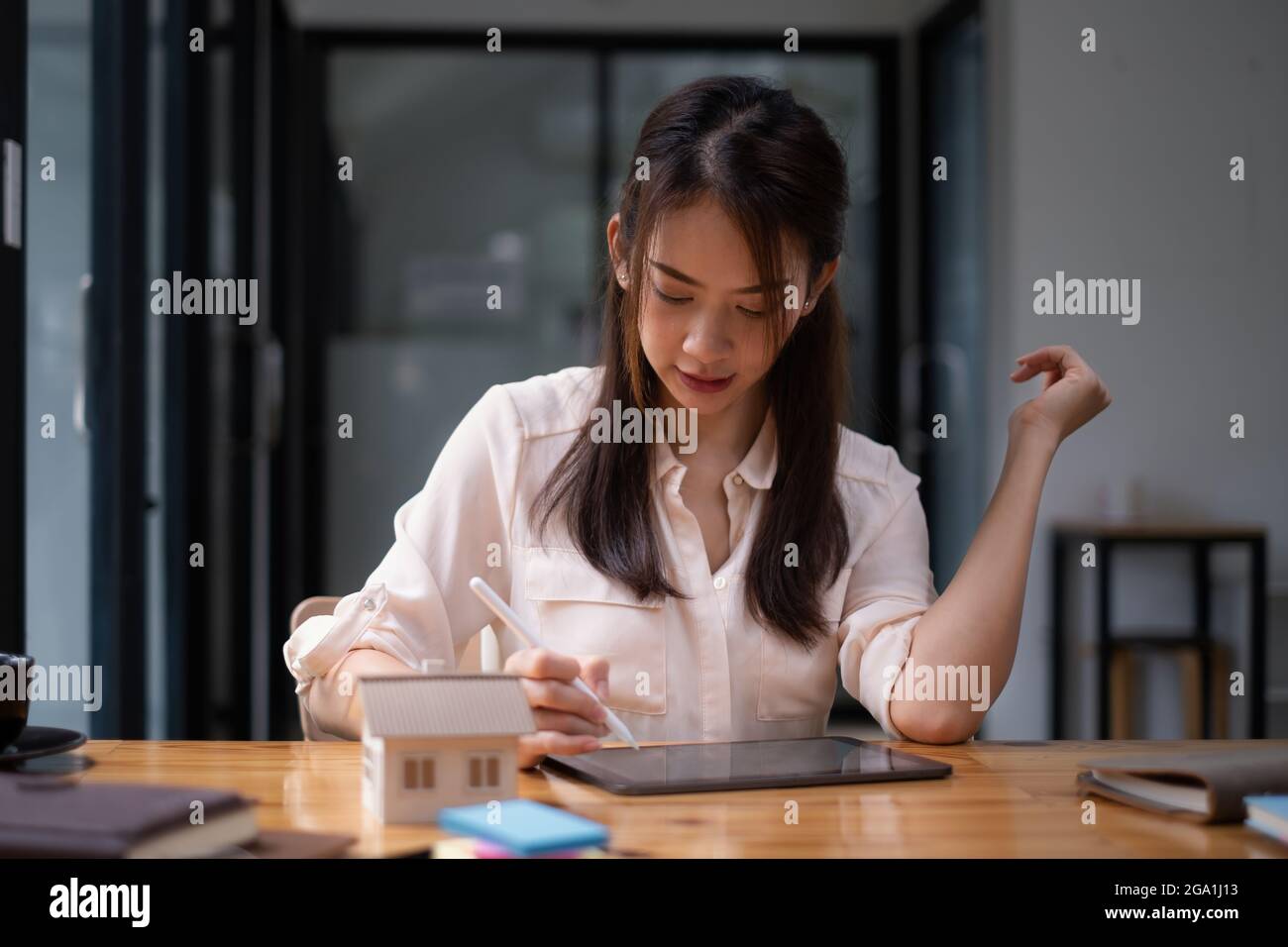 Donna architetto che utilizza un'applicazione tablet digitale per disegnare a mano una casa di design con un modello su una scrivania in legno. Idea di immobile in bene immobile. Foto Stock