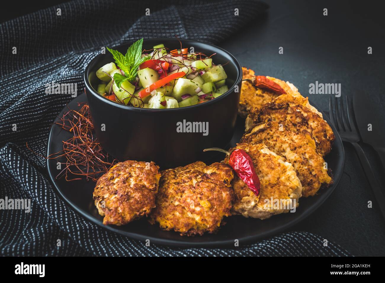 Insalata di cetrioli fresca in una ciotola nera con polpette di pesce o verdure o polpette intorno Foto Stock