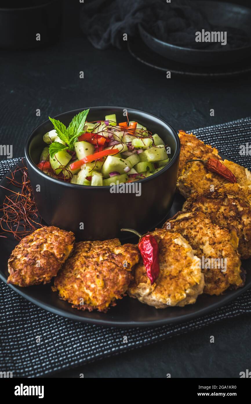 Insalata di cetrioli fresca in una ciotola nera con polpette di pesce o verdure o polpette di carne intorno, verticale Foto Stock