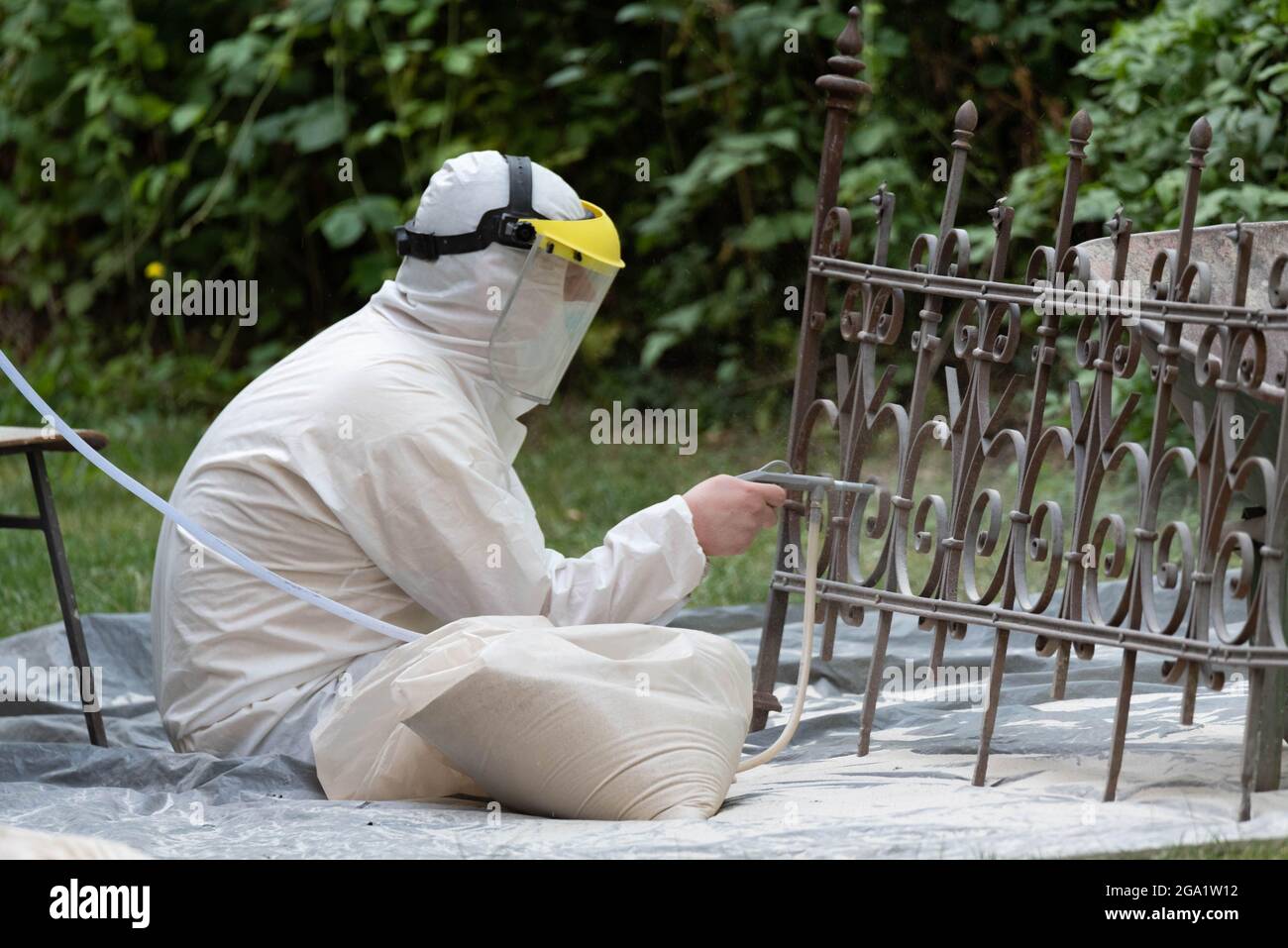 Sabbiatura di una vecchia recinzione metallica. Un uomo in una tuta bianca  e una maschera antipolvere. Pulizia e restauro di elementi metallici Foto  stock - Alamy