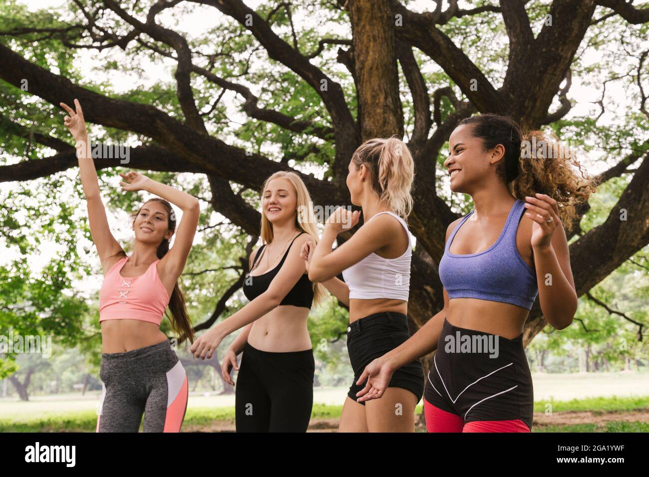 felice giovane multietnica donne adolescenti amici gruppo rilassarsi e ballare dopo l'esercizio nel parco al fine settimana mattina. vita dopo covid. Foto Stock