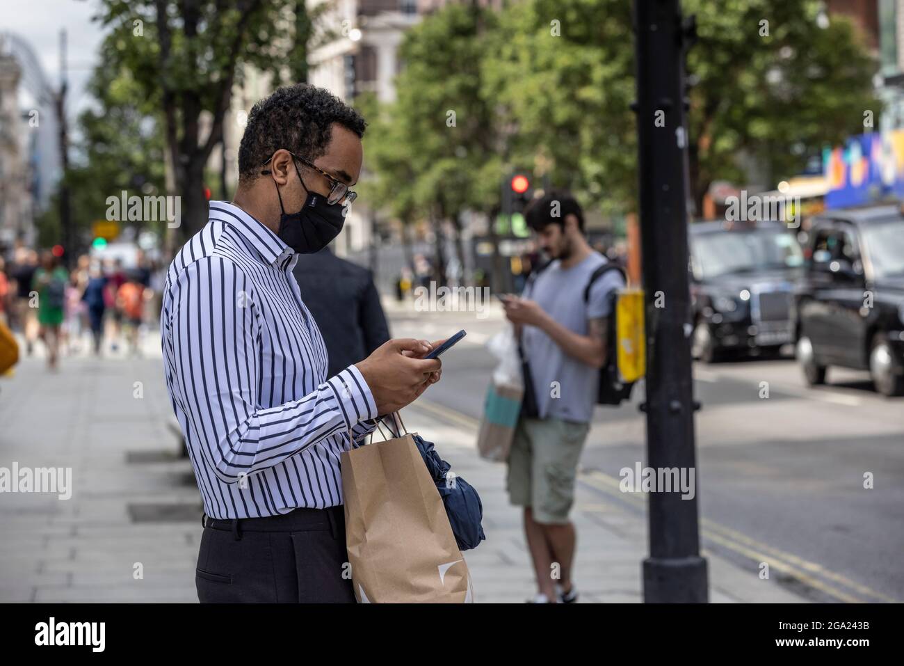 Uomini che usano i loro smartphone mentre fuori su Oxford Street, Londra centrale, Inghilterra, Regno Unito Foto Stock