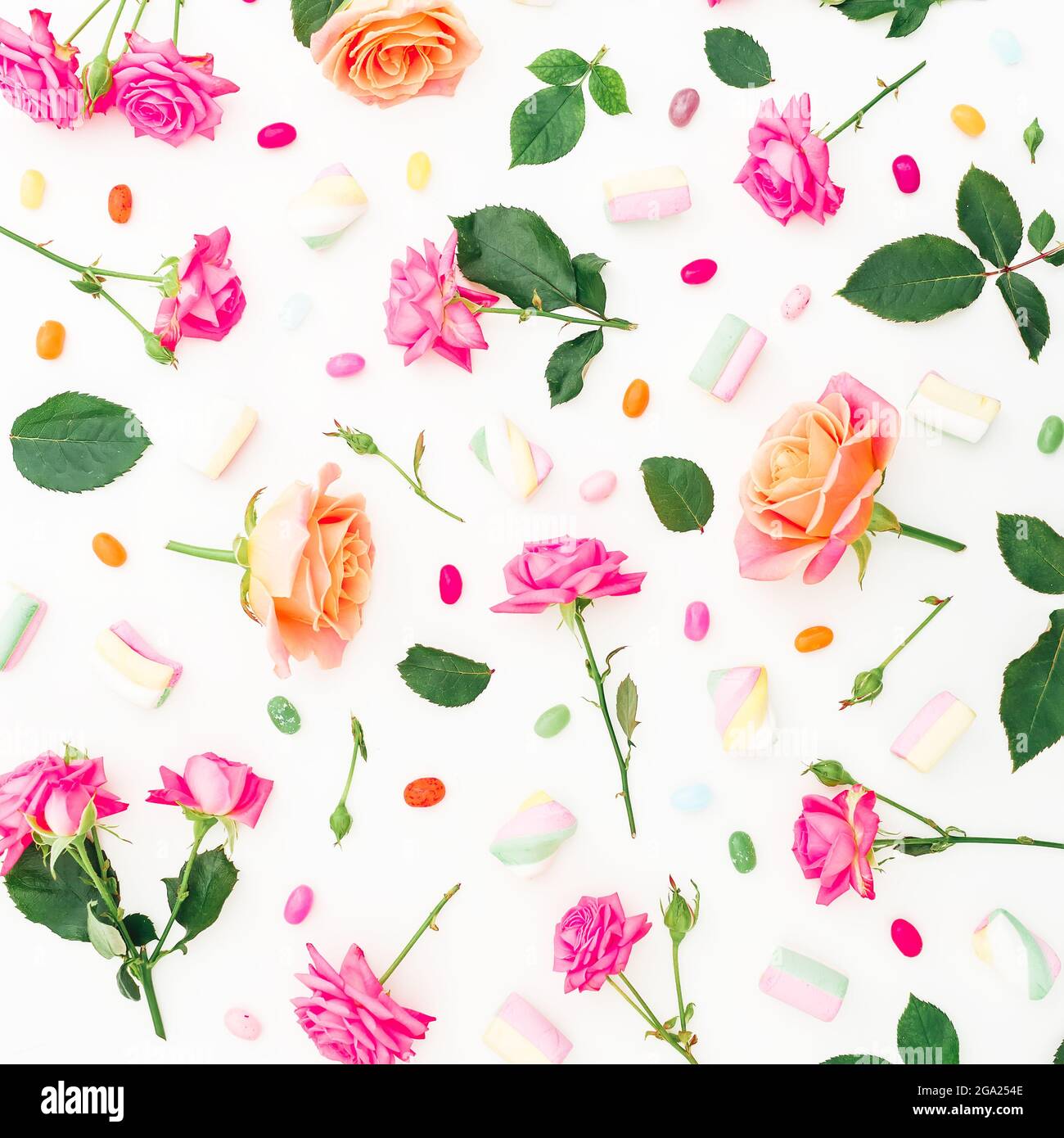 Modello con fiori di rose e foglie con caramella su sfondo bianco. Disposizione piatta, vista dall'alto. Foto Stock