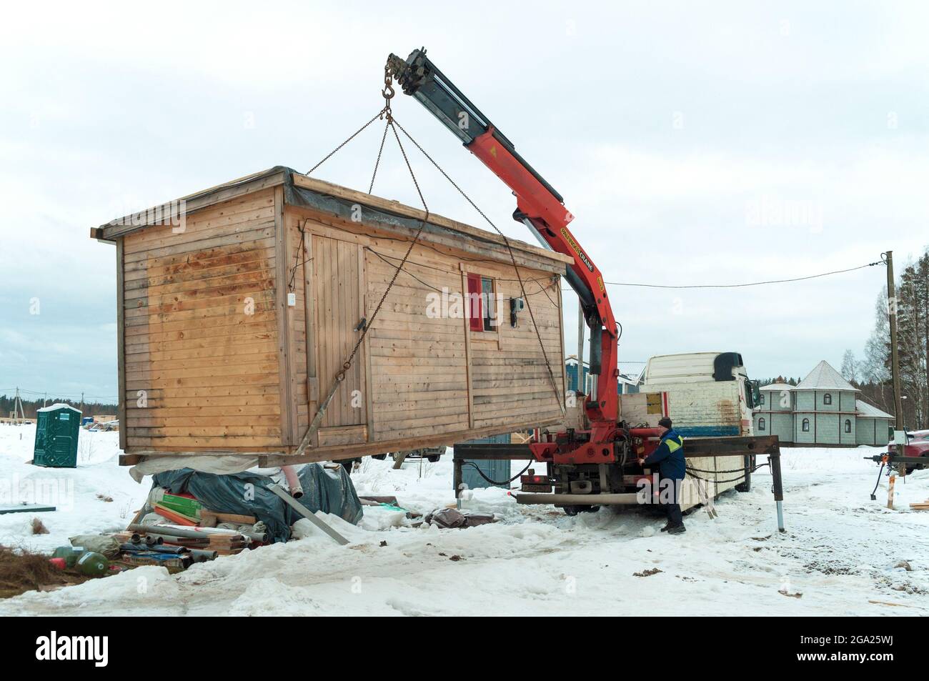 REGIONE DI LENINGRAD, RUSSIA - 04 MARZO 2021: Un camion con un manipolatore di gru carica una casa di costruzione sul sito di costruzione di una casa di campagna Foto Stock