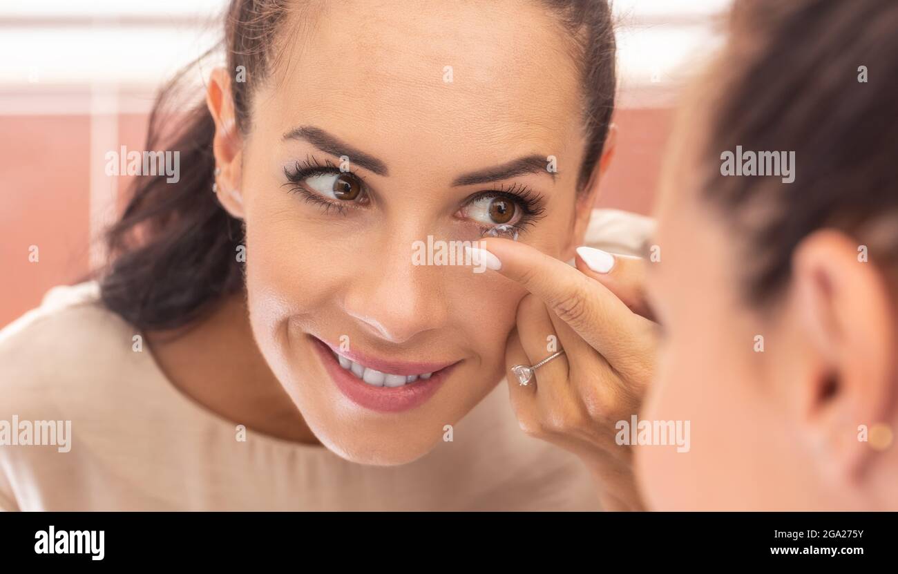 Una giovane donna mette lenti a contatto negli occhi la mattina in bagno di fronte a uno specchio. Foto Stock