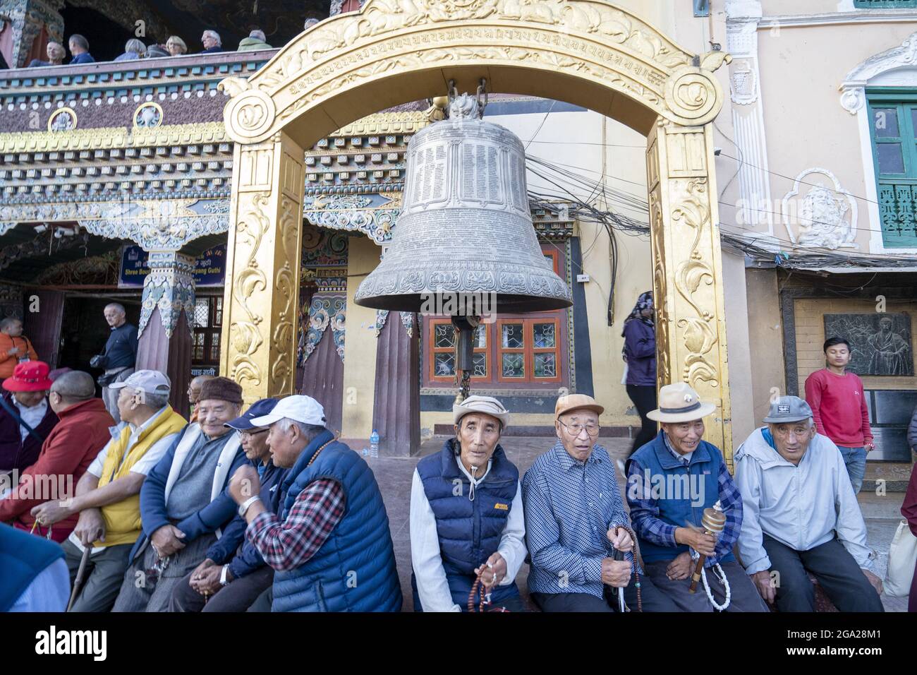 Persone sedute intorno ad una campana nel cortile del più grande stupa buddista tibetano in Nepal a Boudhanath a Kathmandu, Nepal Foto Stock