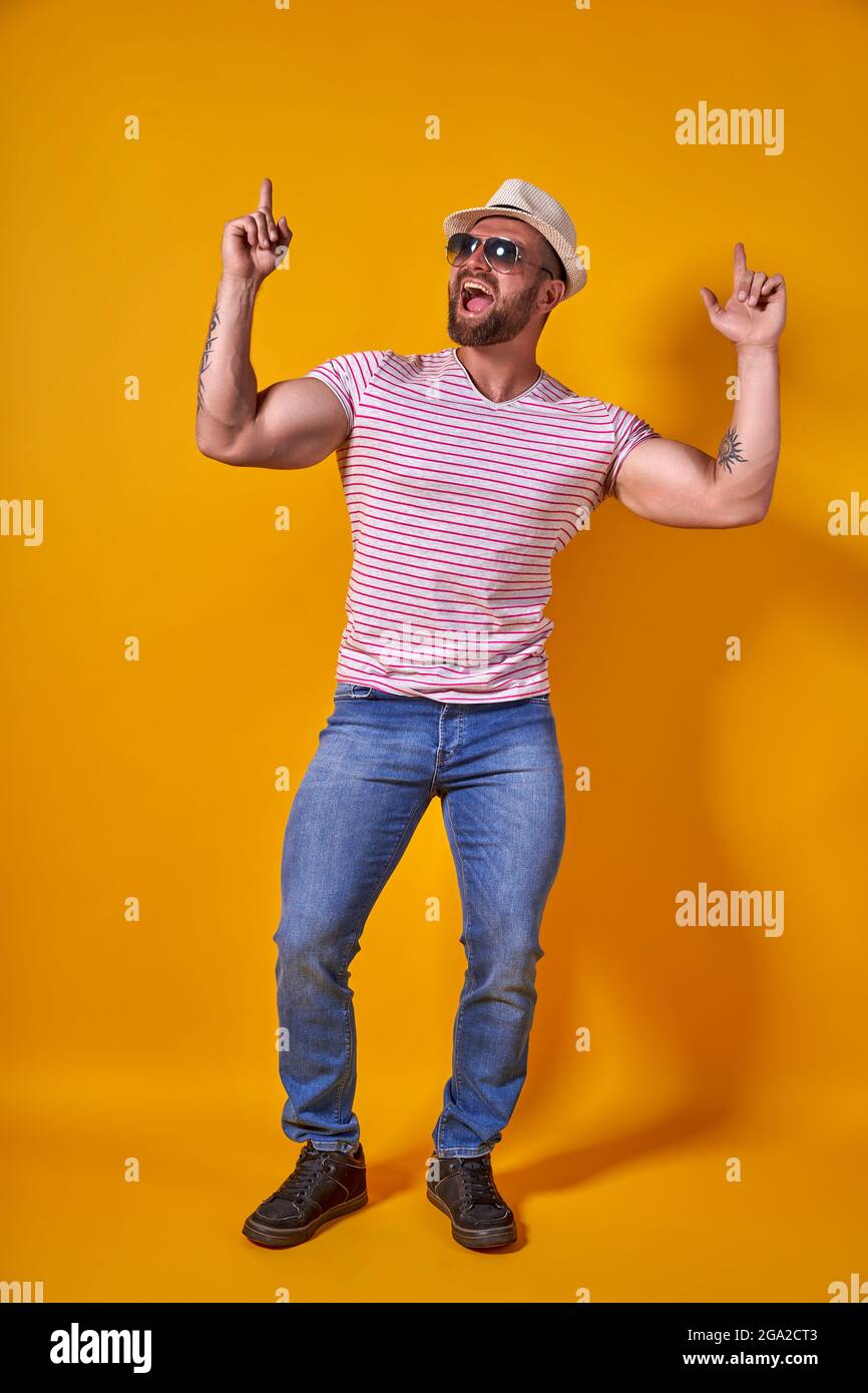Ritratto di ottimista funky ragazzo danza indossare estate look cappello di paglia, occhiali da sole isolato su sfondo giallo Foto Stock