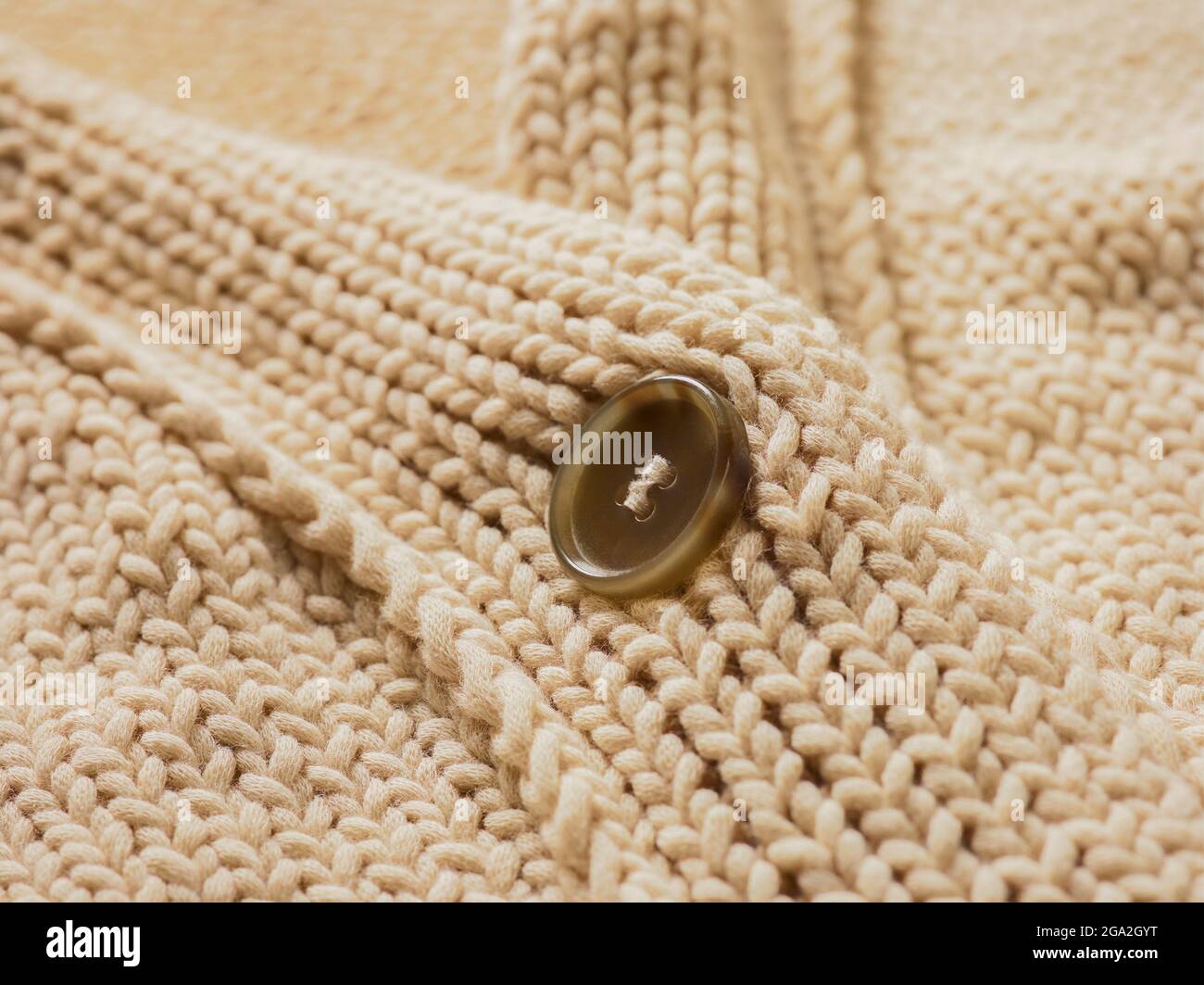Primo piano estremo del colletto e del bottone su un pullover in maglia color crema; studio Foto Stock