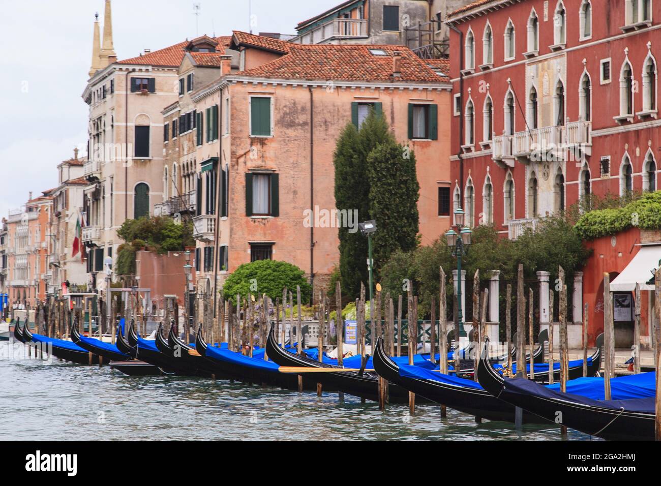 Gondole coperte ormeggiate lungo il canale di fronte a vecchi edifici in pietra; Venezia, Italia Foto Stock